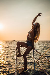 Full length of woman with arms raised in sea against sky