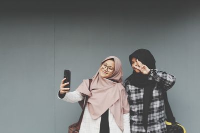 View of young women taking selfie by wall outdoors