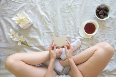 Low section of woman holding placard while sitting with breakfast and gift on bed