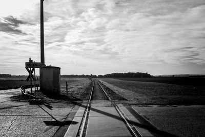 Railroad tracks amidst field against cloudy sky