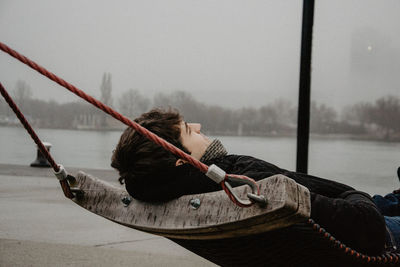 Man sitting on boat against lake against sky