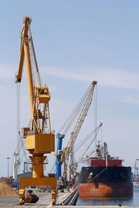 Cranes at harbor against sky