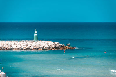 Lighthouse by sea against blue sky