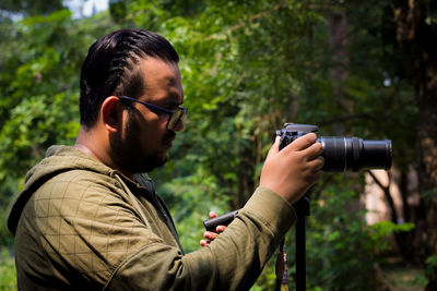 Side view of man photographing with camera in forest