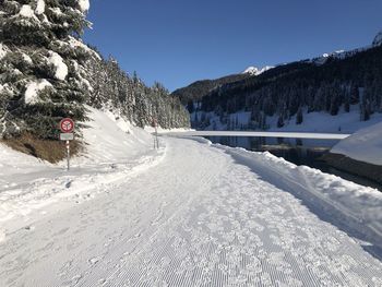 Snow covered road by mountains against clear sky