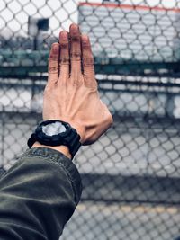 Cropped image of hands against chainlink fence