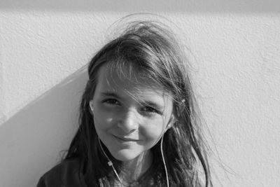 Close-up portrait of girl listening music against wall