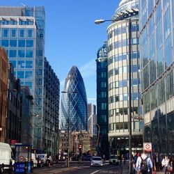 Road amidst modern buildings in city on sunny day