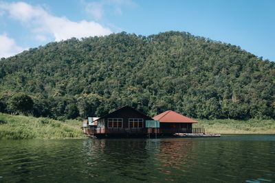 House amidst plants and trees by lake against sky