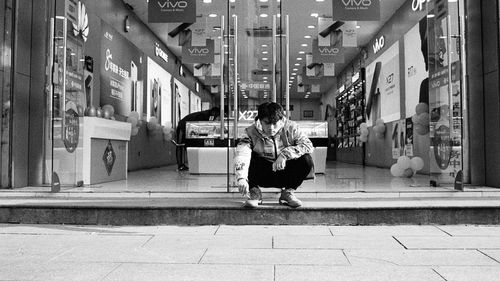 Man sitting on footpath amidst buildings in city