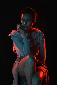 Portrait of young woman sitting against black background