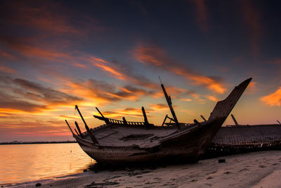 Silhouette boat moored on beach against sky during sunset