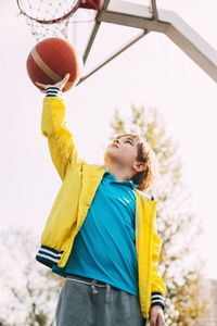 Low angle view of boy playing basketball in court