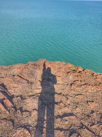 Shadow of person on rock by sea