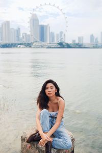 Portrait of beautiful young woman sitting or rock by sea