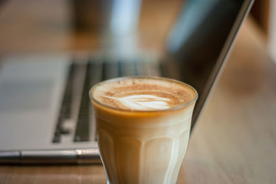 A cup of coffee latte with beautiful latte art. on the wood table near a notebook with the sunlight.