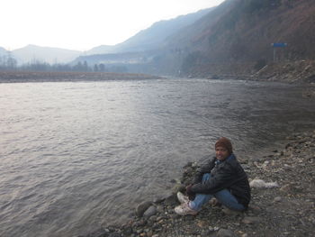 Man sitting on riverbank against sky