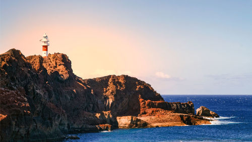 Lighthouse by sea against sky