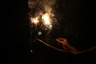 Midsection of person holding illuminated sparklers at night