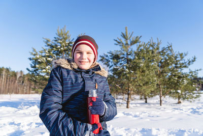 Portrait of smiling young woman standing on snow covered field against sky