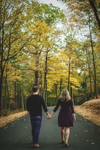 Rear view of friends walking on road in forest