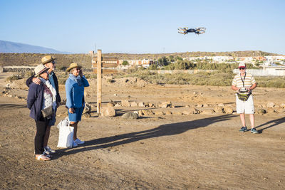 Full length of friends looking at drone while standing on mountain against sky