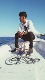 Full length of man sitting by sea against clear sky