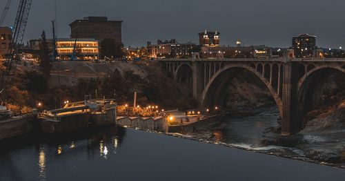 Illuminated bridge over river against sky in city at night