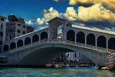 Arch bridge over river against cloudy sky