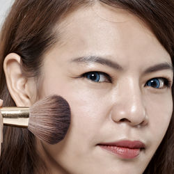 Portrait of woman applying make-up with brush against gray background