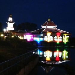 Illuminated building by river against sky at night