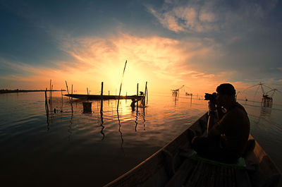 Man photographing sea while sitting in boat against sky