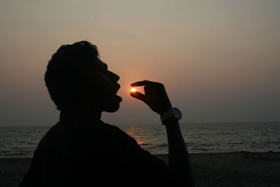 Optical illusion of silhouette men eating sun at sunset