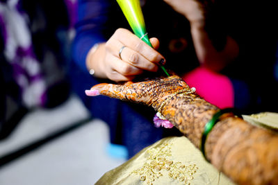 Midsection of woman making henna tattoo on friend palm