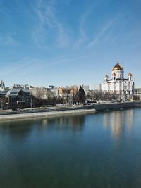 View of buildings by river against blue sky