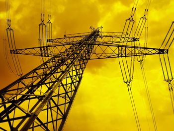 Low angle view of electricity pylon against sky during sunset