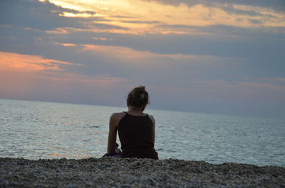 Wife sitting on shore against sky during sunset