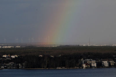 Scenic view of rainbow over sea and buildings against sky