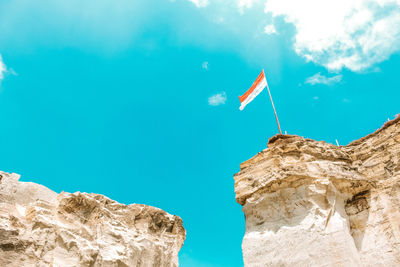 Low angle view of flag on rock against blue sky