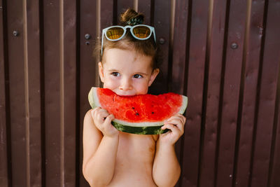 Shirtless girl eating watermelon against wall