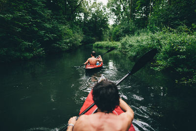 Rear view of shirtless male friends kayaking in river at forest