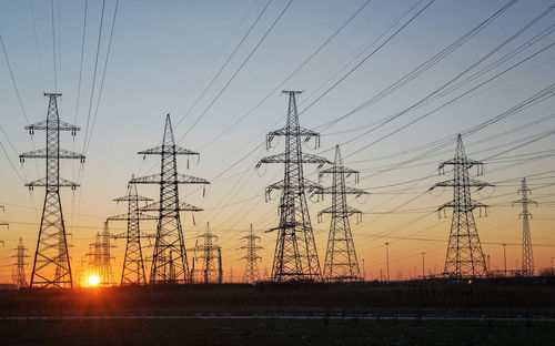 Silhouettes of a high-voltage electric tower against the background of the rising sun and sky. 