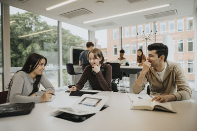 Happy multiracial male and female students studying at table in university