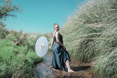 Portrait of young woman standing on field against sky