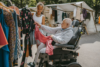 Female owner assisting customer on wheelchair buying dress at flea market