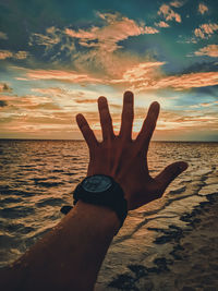 Midsection of person at sea shore against sky during sunset