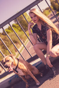 Portrait of young woman sitting by dog on footbridge