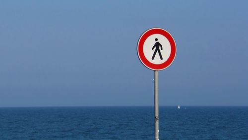 Information sign by sea against clear sky