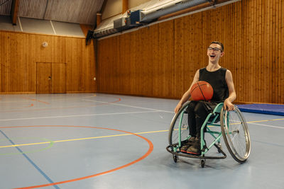 Happy girl with basketball sitting on wheelchair at sports court