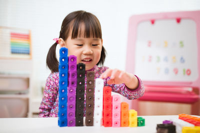 Cute girl stacking toy blocks on table at home